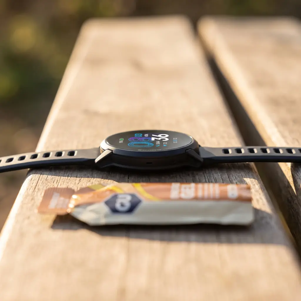 Side view of a thin GPS watch next to an energy gel.