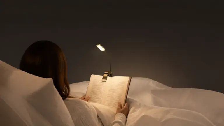 An adult reading in bed at night using a small clip-on book light. - best reading lights for books in bed